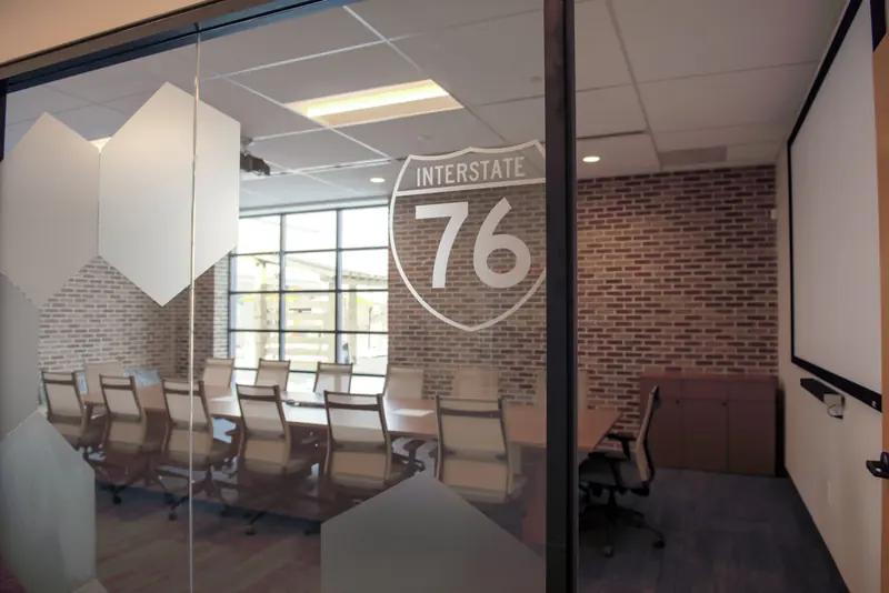 Glass-walled conference room with an Interstate 76 shield and an exposed brick wall