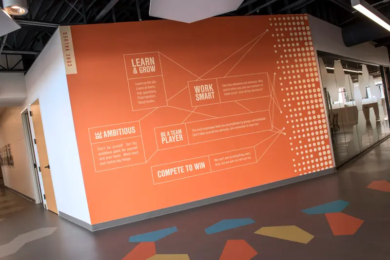 Orange core values wall graphic with a dot pattern above colorful floor tiles