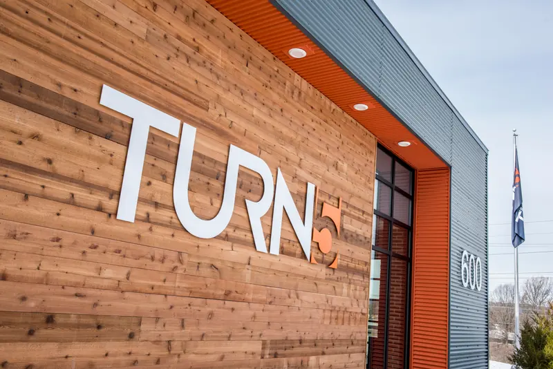 Turn5 logo in white letters on a cedar-clad entrance wall with an orange soffit