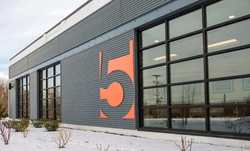 Gray metal-clad wall with a large orange 5 and black-framed windows in the snow