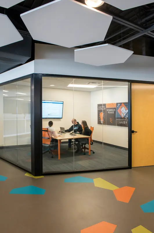 Small glass-walled huddle room under hexagonal ceiling baffles