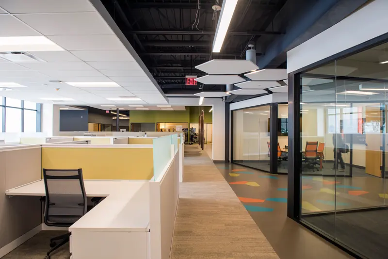 Open office with low cubicle walls, glass-walled rooms and a colorful floor inlay
