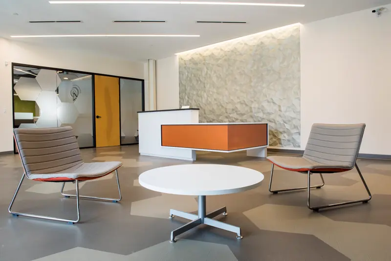 Lounge seating and a round table in front of a textured stone wall and the reception desk