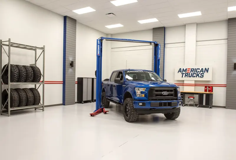 Studio bay with a blue pickup truck on a lift and an American Trucks sign