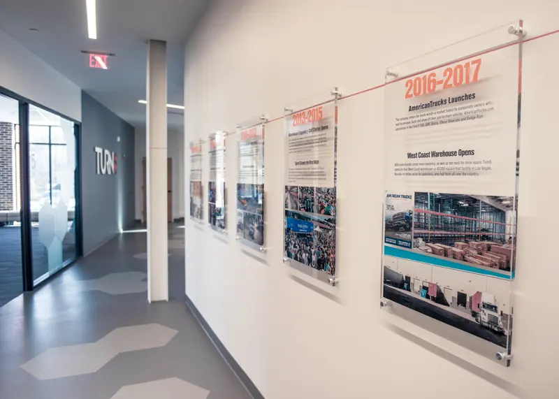 Company timeline panels mounted on a hallway wall with hexagon floor tiles