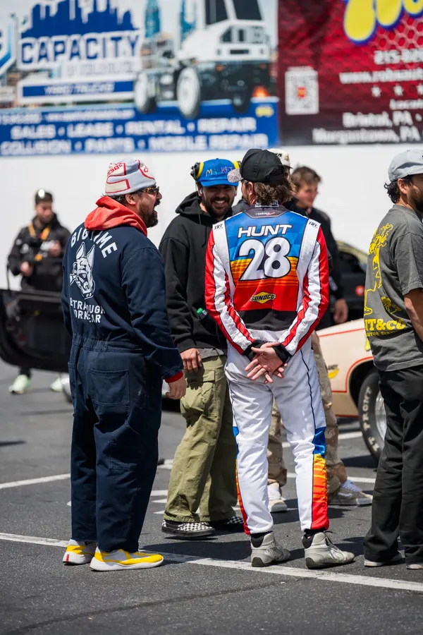 Two creators in work gear and a race suit talking in the staging area at the track