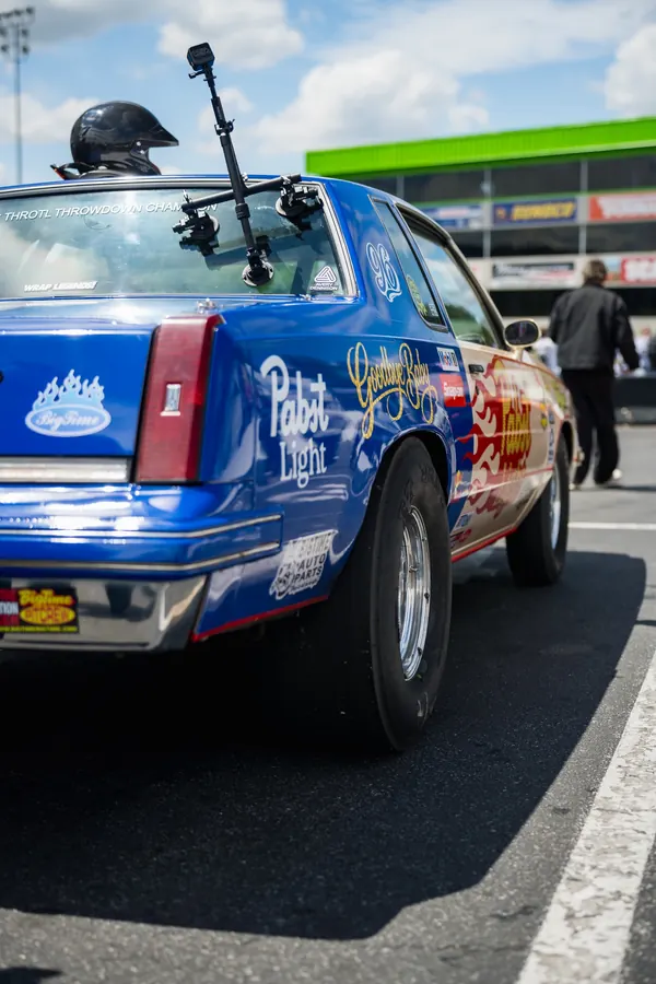 A blue and tan drag car with a throtl Throwdown champion windshield banner and roof camera mount