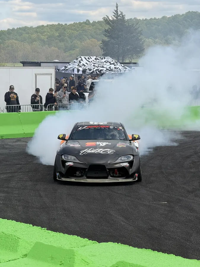 A black Toyota Supra drifting through tire smoke in the burnout box with fans filming